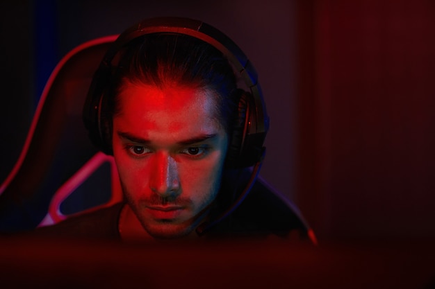 A high-contrast photo of an esports player intensely focused, illuminated by the glow of multiple monitors, capturing the pressure and dedication of competitive gaming.