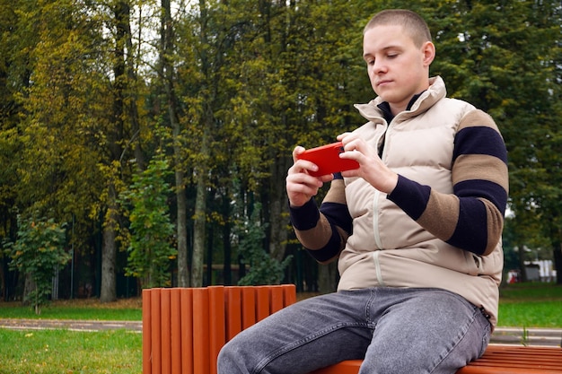 A person is holding a Nintendo Switch console while sitting on a park bench. The screen displays a streaming app interface, and there are trees and greenery in the blurred background, emphasizing the console's portability and potential for outdoor entertainment.