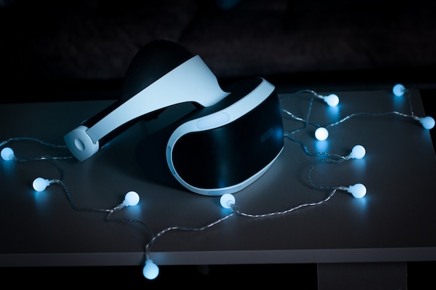 A sleek and modern image of the PlayStation VR2 headset, showcasing its design and ergonomic features. The headset is displayed on a stand, with a PlayStation 5 console subtly visible in the background. The image highlights the high-resolution lenses and integrated headphones of the VR headset.