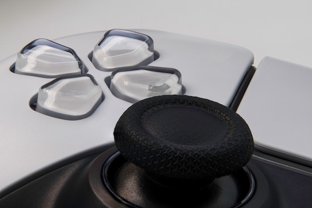 Close-up of a gaming console controller with various buttons and ergonomic design elements, with a blurry gamer using it in the background.