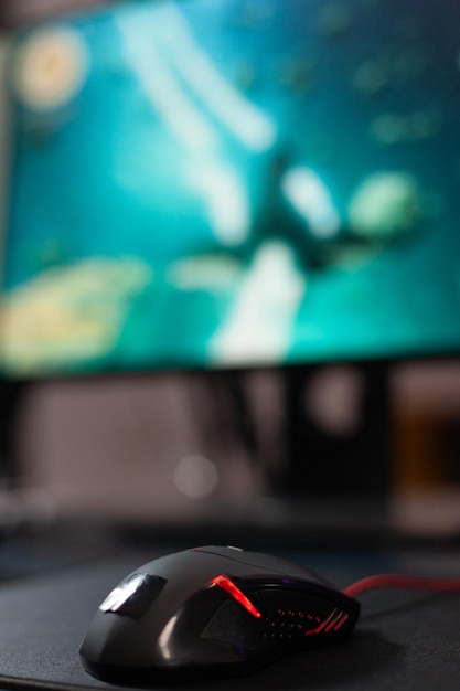 A close-up shot of a high-quality webcam mounted on a gaming monitor, capturing a streamer's face. The background shows a soft, blurred gaming setup with various peripherals.